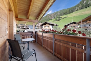 A wooden balcony with a table and chairs, overlooking a mountainous landscape.