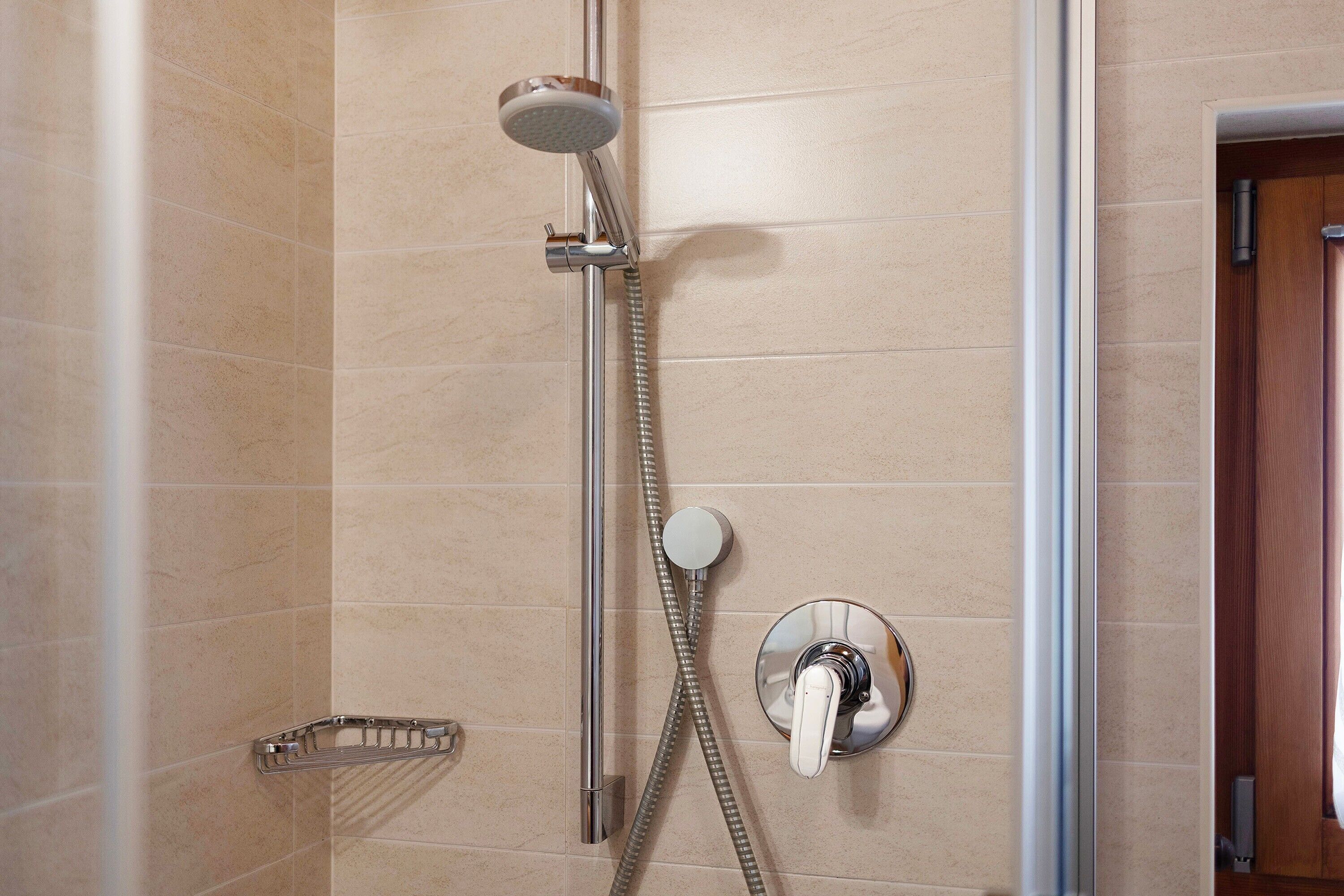 Eine Dusche mit Duschbrause, Wandarmatur und einer Chrom-Armaturenleiste.