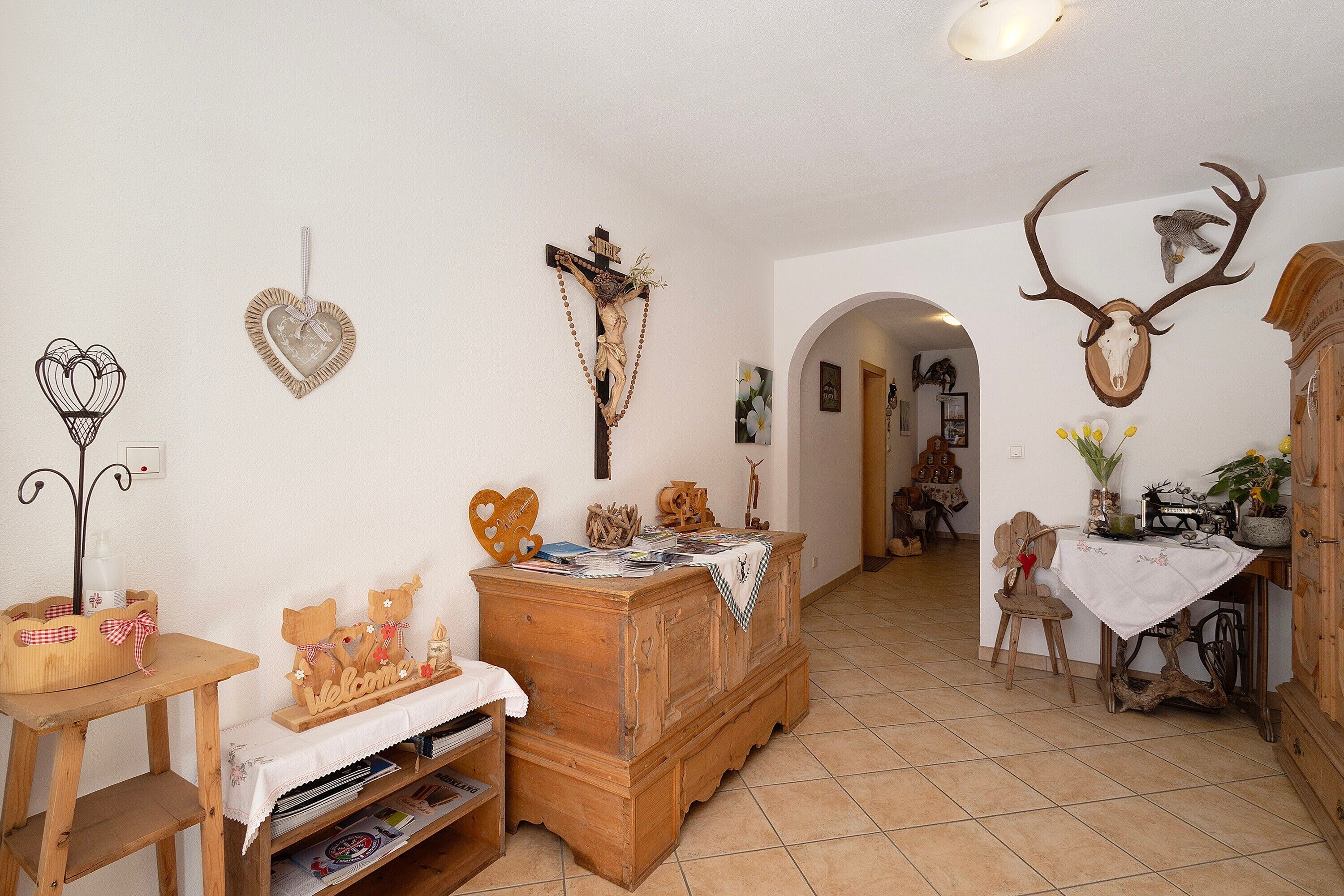 A rustic interior with a wooden dresser, a heart-shaped decoration, a crucifix, and a deer skull mounted on the wall.