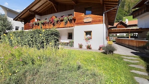 Una cabaña de madera con balcón, rodeada de abundante vegetación y un cielo despejado.