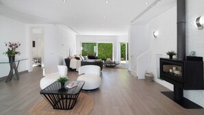 A modern living room with a fireplace, white walls, and a dining area with a glass table. - Villa "Pine Lodge" gated residence with heated private pool (Vilamoura)