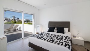 A modern bedroom with a large bed, a nightstand, a dresser, and a balcony with chairs. - Villa "Pine Lodge" gated residence with heated private pool (Vilamoura)