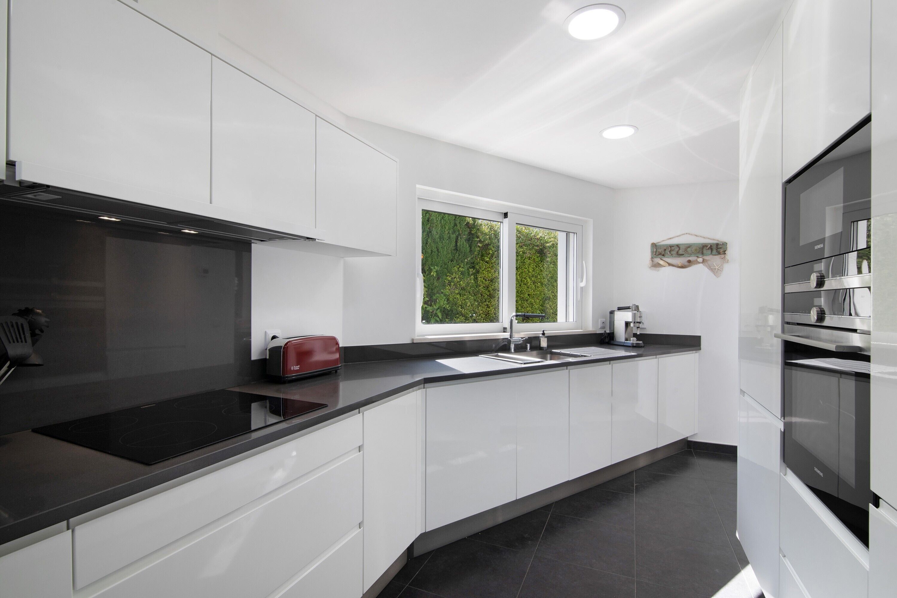 A modern kitchen with white cabinets, a black countertop, a built-in oven, and a window with a view of greenery.