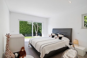 A bedroom with a bed, a nightstand, a window, and a view of greenery outside.