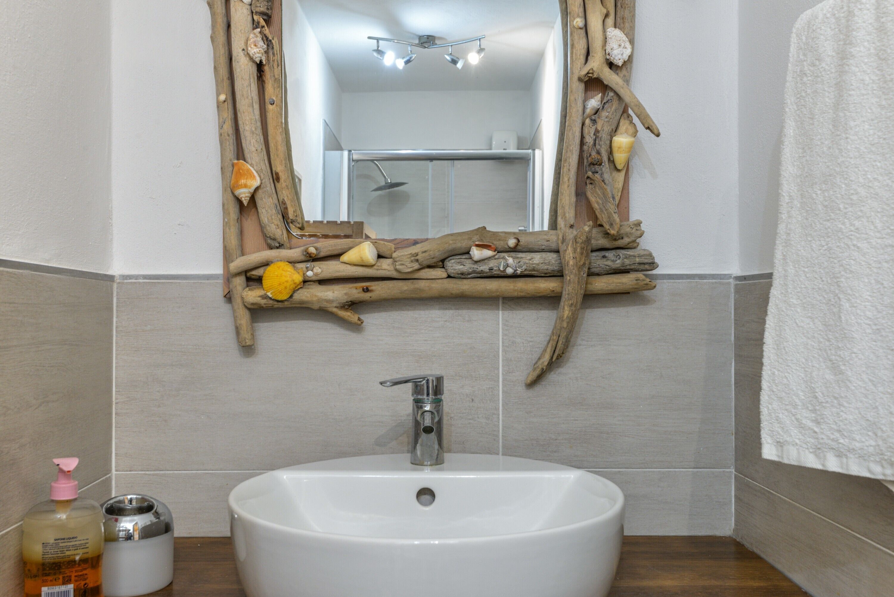 A bathroom with a white sink, a mirror with a wooden frame, and a shower visible in the background.