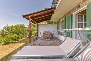 Un patio cubierto con una mesa, sillas y una tumbona, con suelo de piedra.