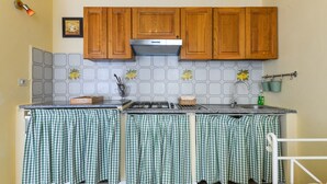 A kitchen with wooden cabinets, a stainless steel range hood, a tiled backsplash, and a checkered cloth covering the countertop. - Apartment "Il Girasole" with Sea View, Private Terrace and Wi-Fi (Marciana)