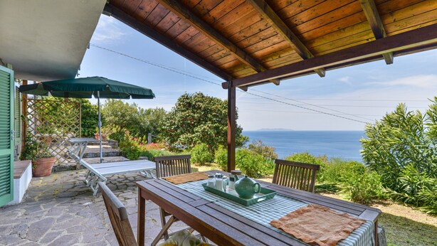 A covered patio with a table set for two, a view of the sea, and a wooden ceiling. - Apartment "Il Girasole" with Sea View, Private Terrace and Wi-Fi (Marciana)