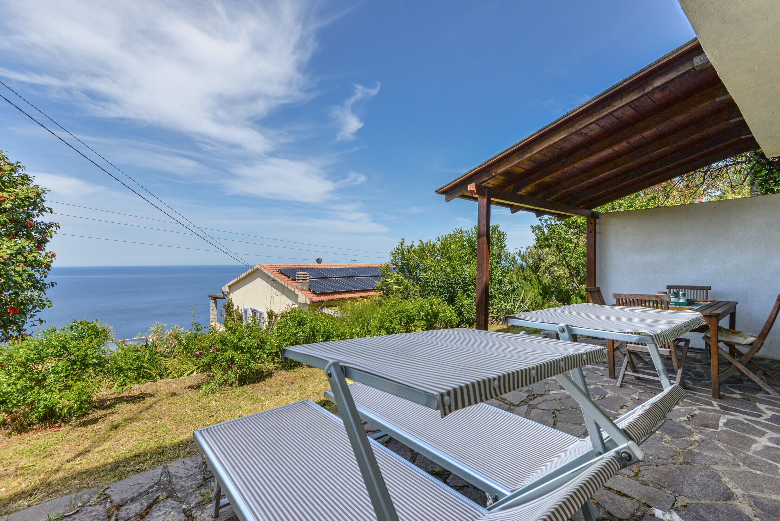 Une terrasse avec des tables et des chaises en métal, un sol en pierre et une vue sur la mer.