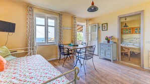 A room with a bed, a dining table with chairs, a small desk, and a window with curtains. - Apartment "Il Girasole" with Sea View, Private Terrace and Wi-Fi (Marciana)