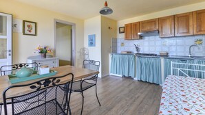 A kitchen with wooden cabinets, a dining table with chairs, and a bed with a floral bedspread. - Apartment "Il Girasole" with Sea View, Private Terrace and Wi-Fi (Marciana)
