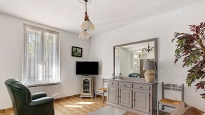 Una sala de estar con un sofá, una silla, un televisor, un mueble aparador y un espejo grande.