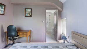 Un dormitorio con cama, escritorio, silla, lámpara y puerta que da al baño.