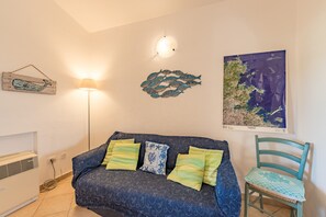 Ett rum med en mönstrad soffa, en fiskdekoration som hänger på väggen, en lampa, en karta och en stol.