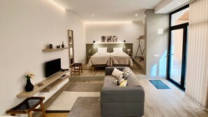 A modern hotel room with a sofa, a TV, a bed with two pillows, a small table, and a mirror. - Apartment 'Ladomar Avenida' with Private Terrace, Private Garden and Wi-Fi (Horta)