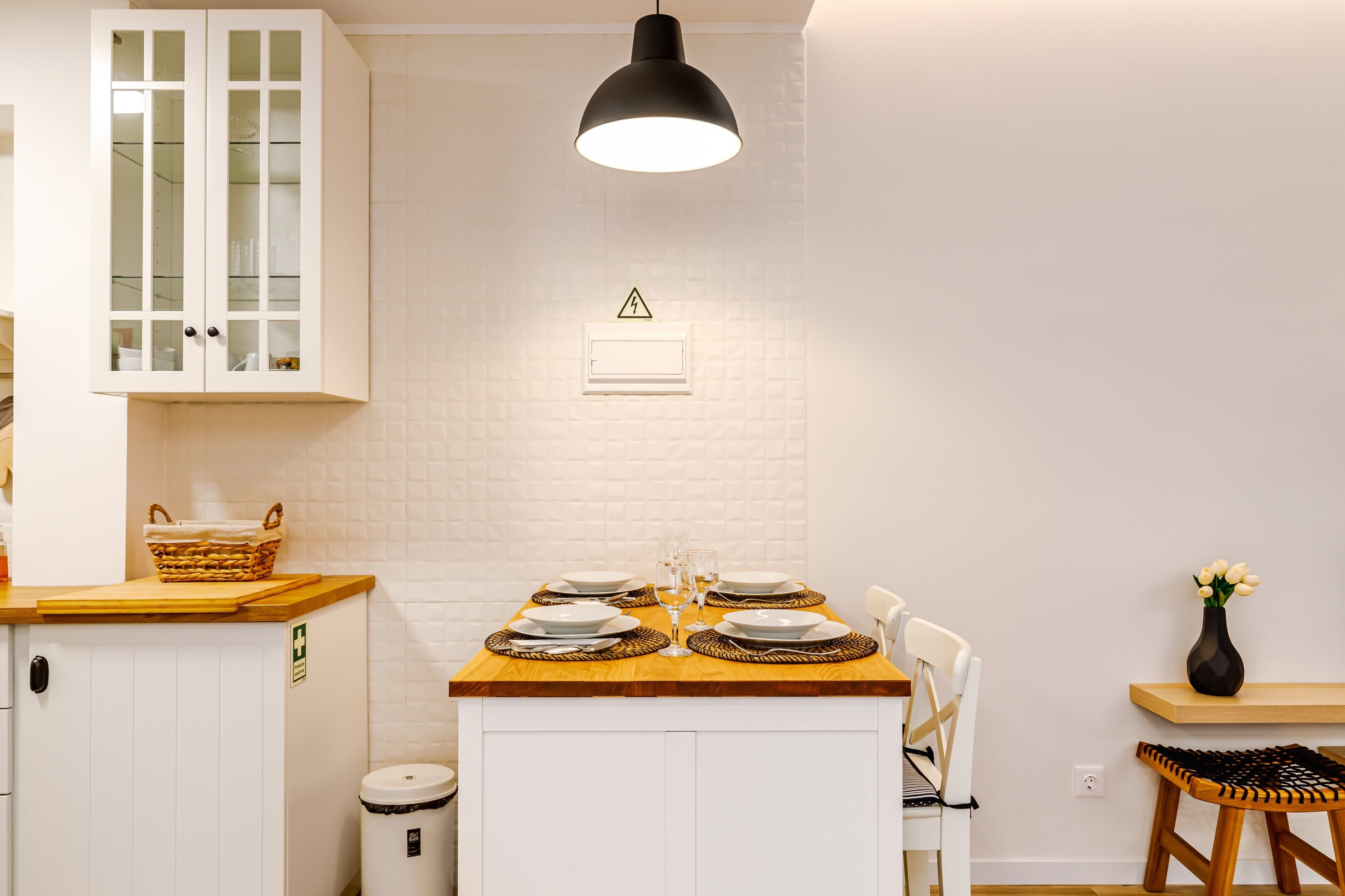 Un coin repas avec une table dressée pour quatre personnes, un panier posé sur le comptoir et une poubelle.