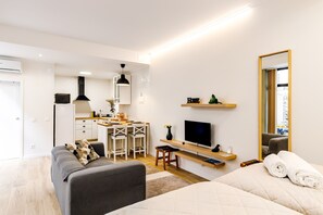 Ein modernes Hotelzimmer mit Küchenzeile, einer Sitzecke, einem Bett, einem Fernseher und einem Spiegel.