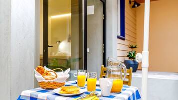A breakfast table with a checkered tablecloth, a basket of croissants, a plate of waffles, glasses of orange juice, and a pitcher.
