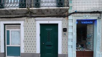 Un edificio con puerta verde, una tienda con cartel que dice 'VAIDADE' y una pared de azulejos con diseño decorativo.