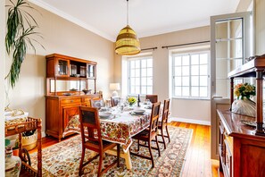 A dining room with a wooden table set for four, a chandelier, and a large window.