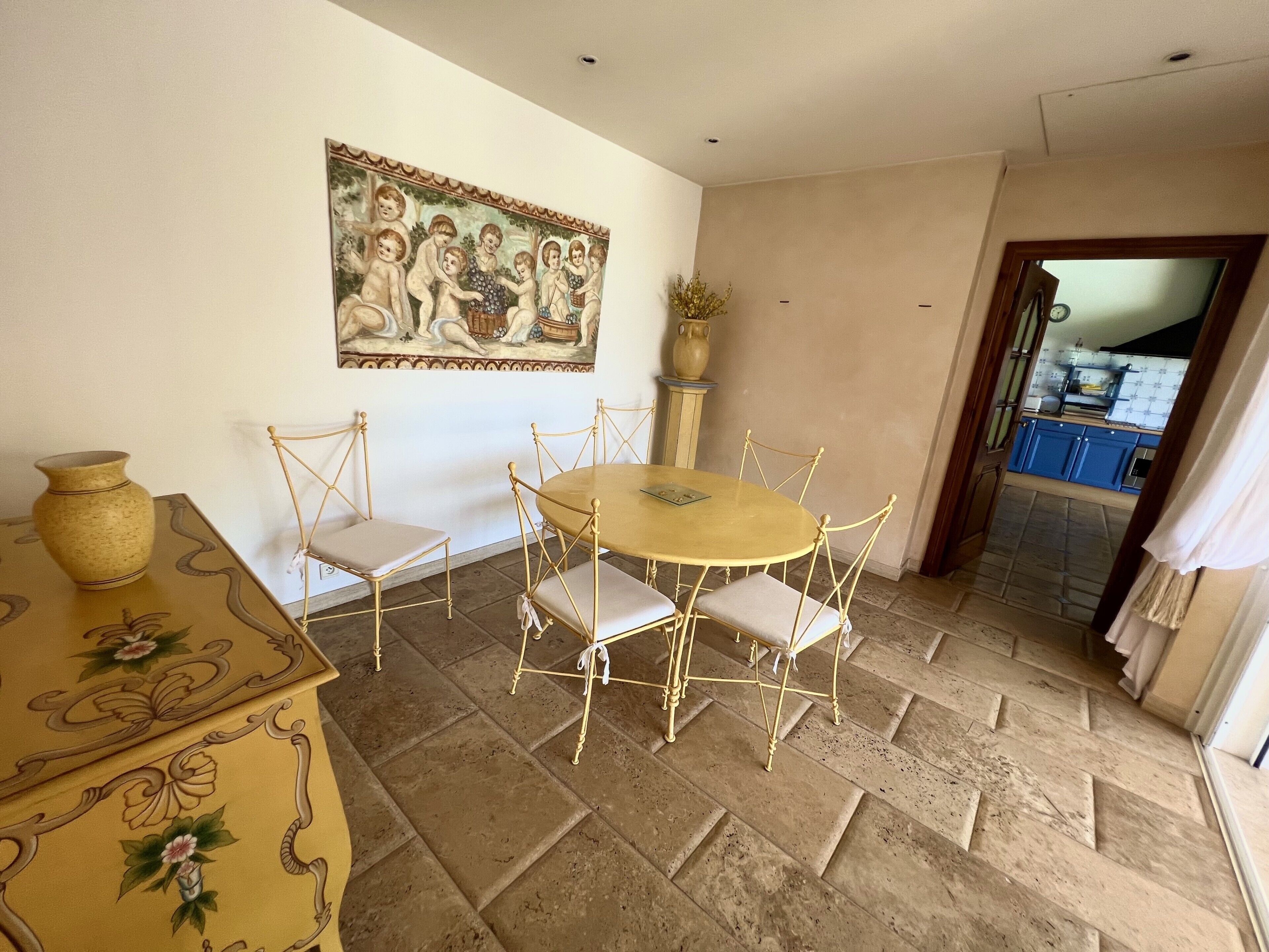 Un coin repas avec une table ronde et six chaises, un vase et un tableau au mur.
