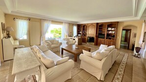 A spacious living room with a fireplace, a dining area, and a kitchen visible through an open door. - Cap d'Antibes - Villa 10 people - Swimming pool (Antibes)
