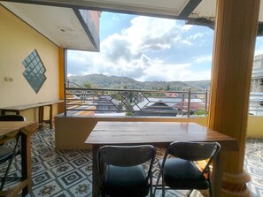 Un balcón con mesa y sillas de madera, suelo estampado y vistas a edificios y colinas.