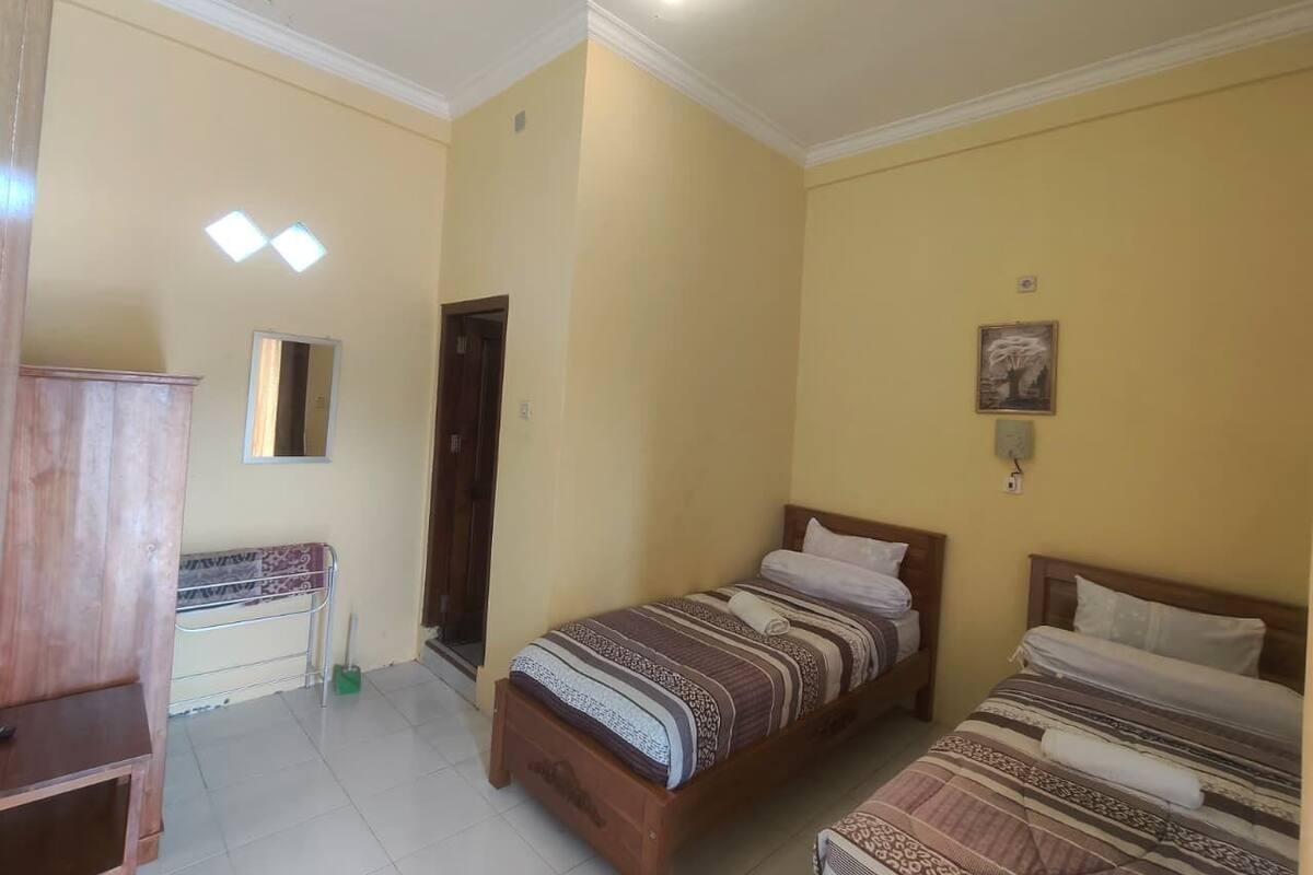 A bedroom with two beds, a wooden wardrobe, a desk with a chair, and a mirror on the wall.