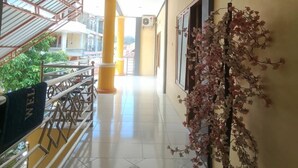Un passadís amb sòl de rajola, pilars grocs i una planta en test amb flors roses.