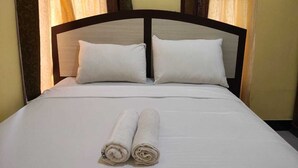 Un llit ben fet amb dues almoines i tovalloles arremolinades, davant d'un fons de cortines amb dibuixos.