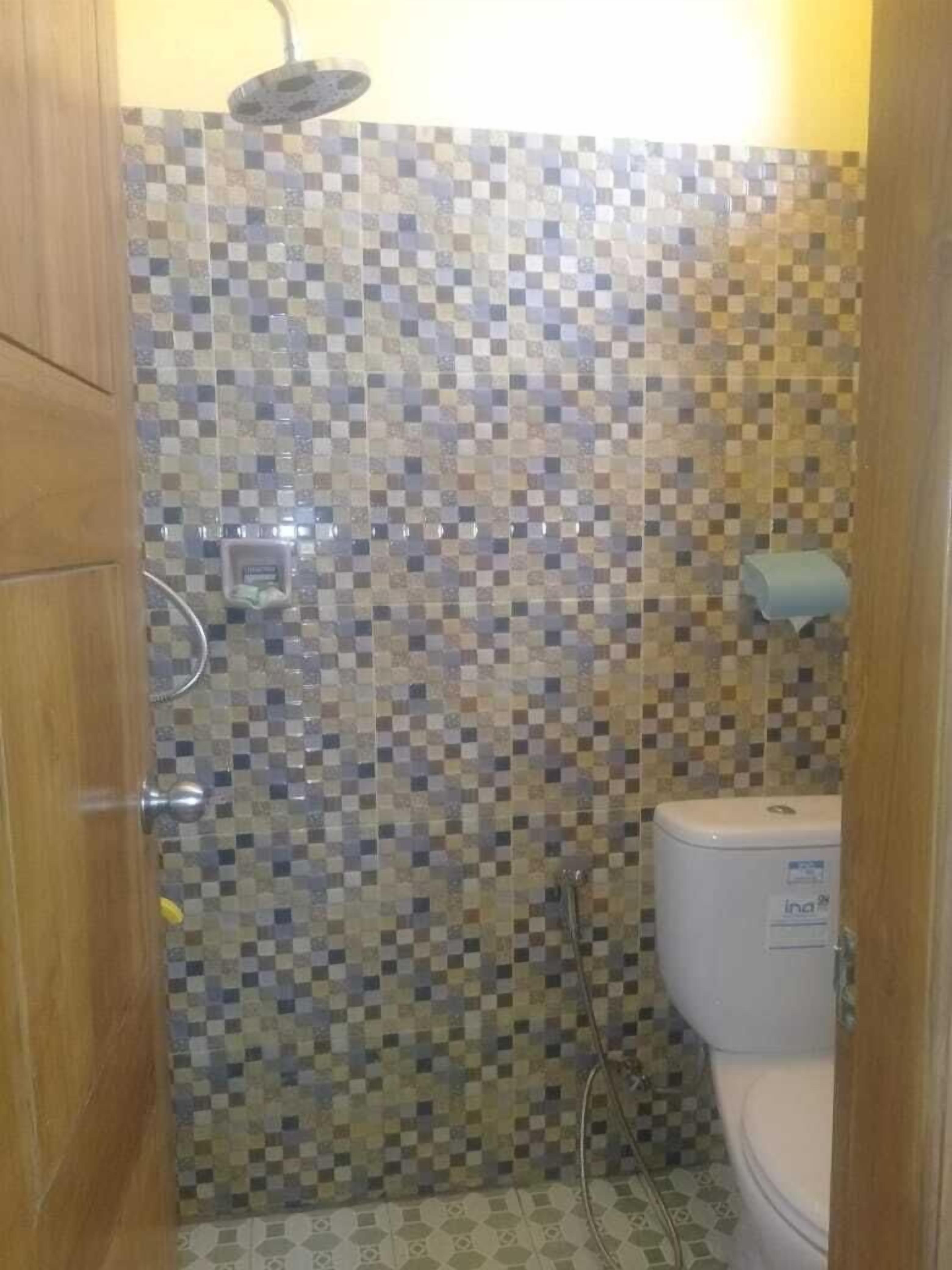 A bathroom with a checkered tile wall, a toilet, and a shower area.