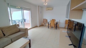 A living room with a sofa, a coffee table, a TV, and a dining area with chairs and a table. - ACV - Torremar-2ª Linea Planta 5 Frontal 2 (OROPESA)