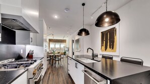 A modern kitchen with stainless steel appliances, a central island with a sink, and a dining area with a brick wall and large windows. - Loft Style Spacious Lux Apt 102, sleeps 6 (Atlanta)