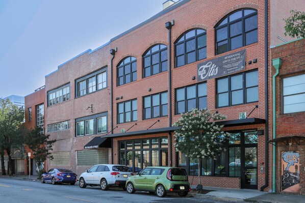 A red brick building with large windows and a sign advertising residential lofts for sale.