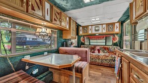 Interior compacto de una caravana con comedor, kitchenette y ventana con vista a un caballo.