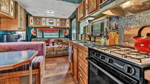 Cocina compacta de autocaravana con armarios de madera, estufa a gas y zona de comedor con banco.