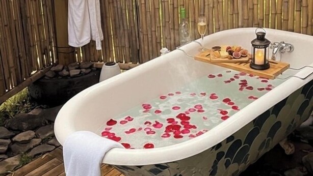 Una bañera al aire libre con pétalos de rosa, una copa de vino y un farol sobre una bandeja.