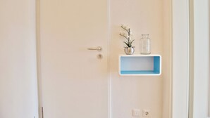 Une porte blanche avec une poignée argentée, une étagère bleue avec une petite plante et une bouteille en verre, et un interrupteur sur le mur.