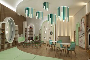 A modern children's play area with circular seating, a central play table, and a wall with colorful storage units. - The Plaza Doha, LXR Hotels & Resorts (DOHA)