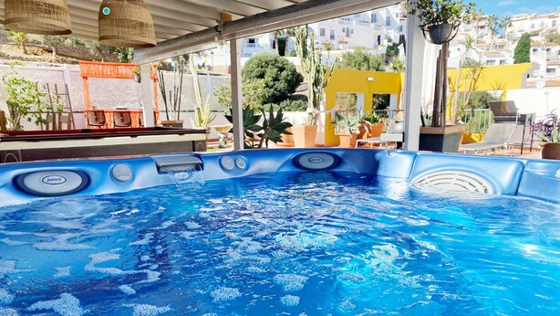 Un bain à remous à l’intérieur bleu, entouré de plantes en pot et de meubles d’extérieur.
