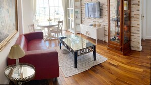 Un salon avec un canapé rouge, une table basse en verre, un meuble blanc et un buffet en bois doté de portes en verre, ainsi qu’un téléviseur fixé au mur.