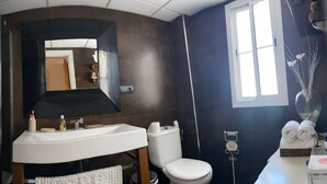 Une salle de bain avec un lavabo blanc, des toilettes, un miroir et une fenêtre.