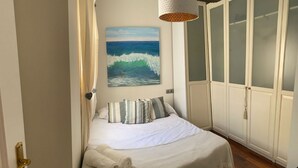Une chambre à coucher avec un lit, un tableau représentant l’océan, une armoire et une porte.