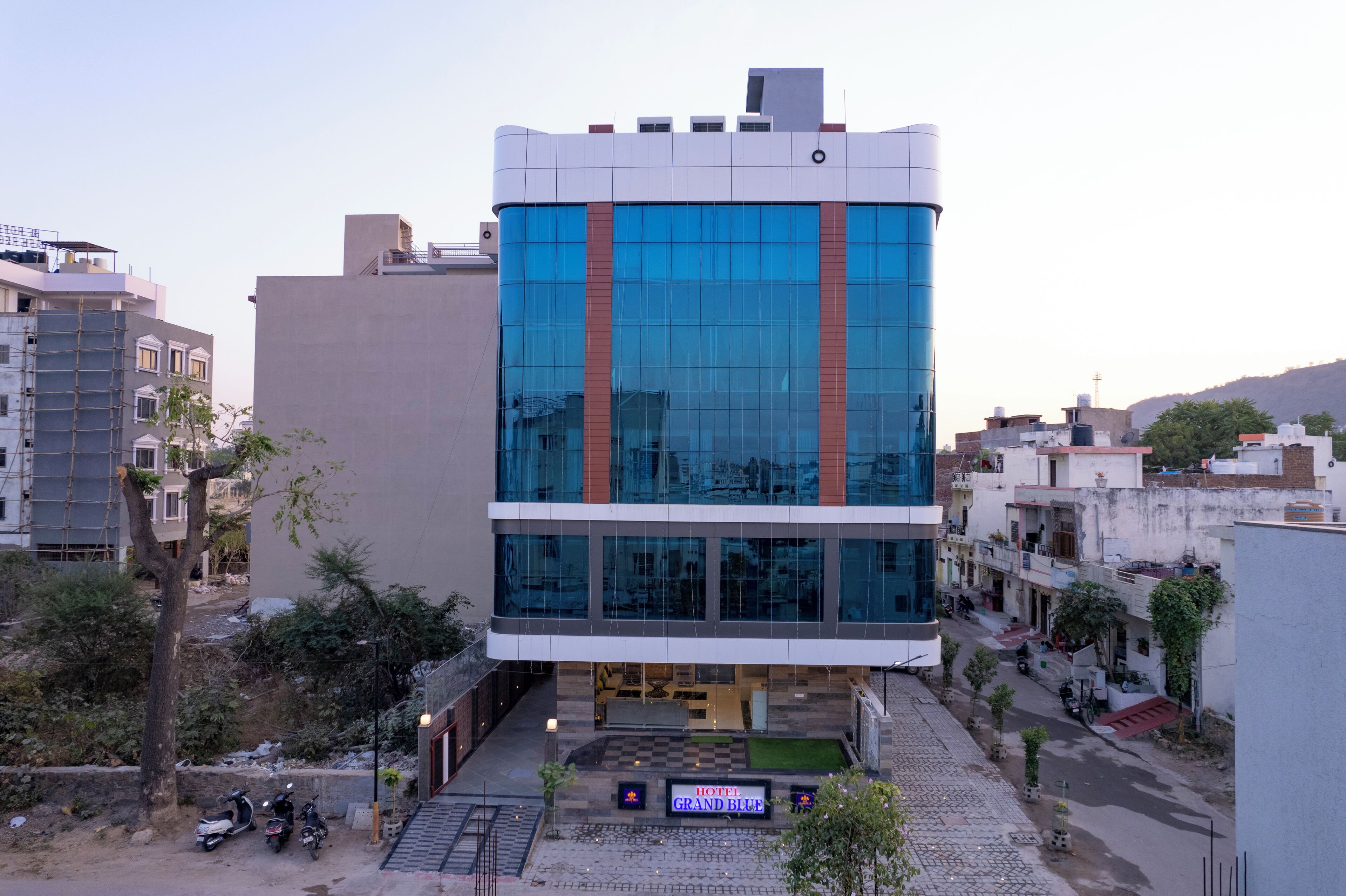 A modern hotel with a glass facade, a checkered entrance, and a sign reading "HOTEL GRAND BLUE".