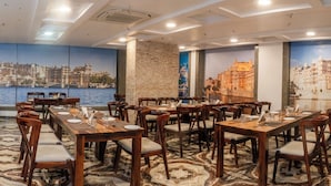 Un comedor con mesas largas, sillas y vistas a un paisaje urbano a través de un ventanal grande.