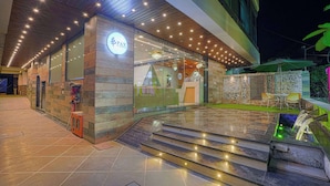 Un edificio moderno con fachada de vidrio, su logo a la vista y un área de entrada bien iluminada con escalones hacia la puerta.