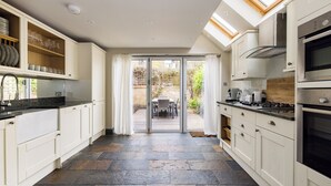 A modern kitchen with white cabinets, a stone tile floor, and a view to a patio with outdoor furniture. - The North Kensington Cottage No.2 (London)
