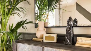 A dark wooden console with geometric patterns, a pink vase, a vintage radio, a black marble sculpture, and a mirror reflecting a plant and a staircase. - The North Kensington Cottage No.2 (London)