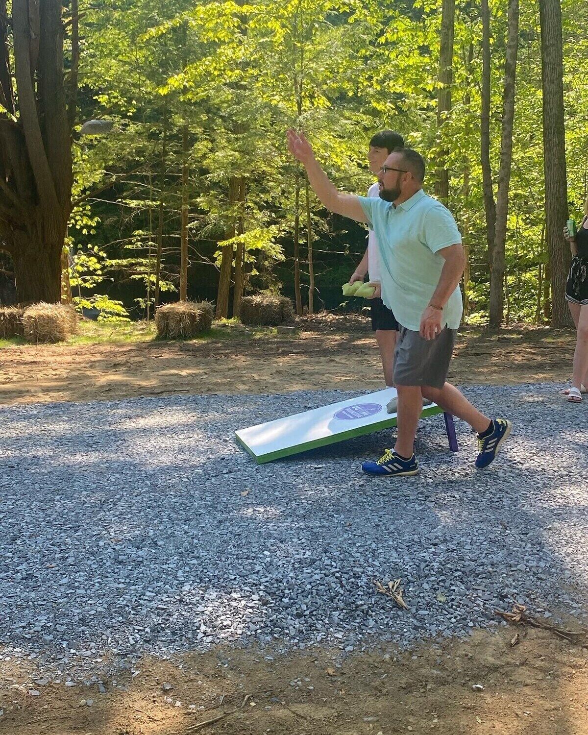 Une personne se tient sur une surface de gravier, avec un tapis devant elle, et est entourée d’arbres.