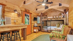 Interior acogedor de una cabaña con detalles de madera, una zona de bar con taburetes, un espacio de estar cómodo y un televisor montado en la pared.